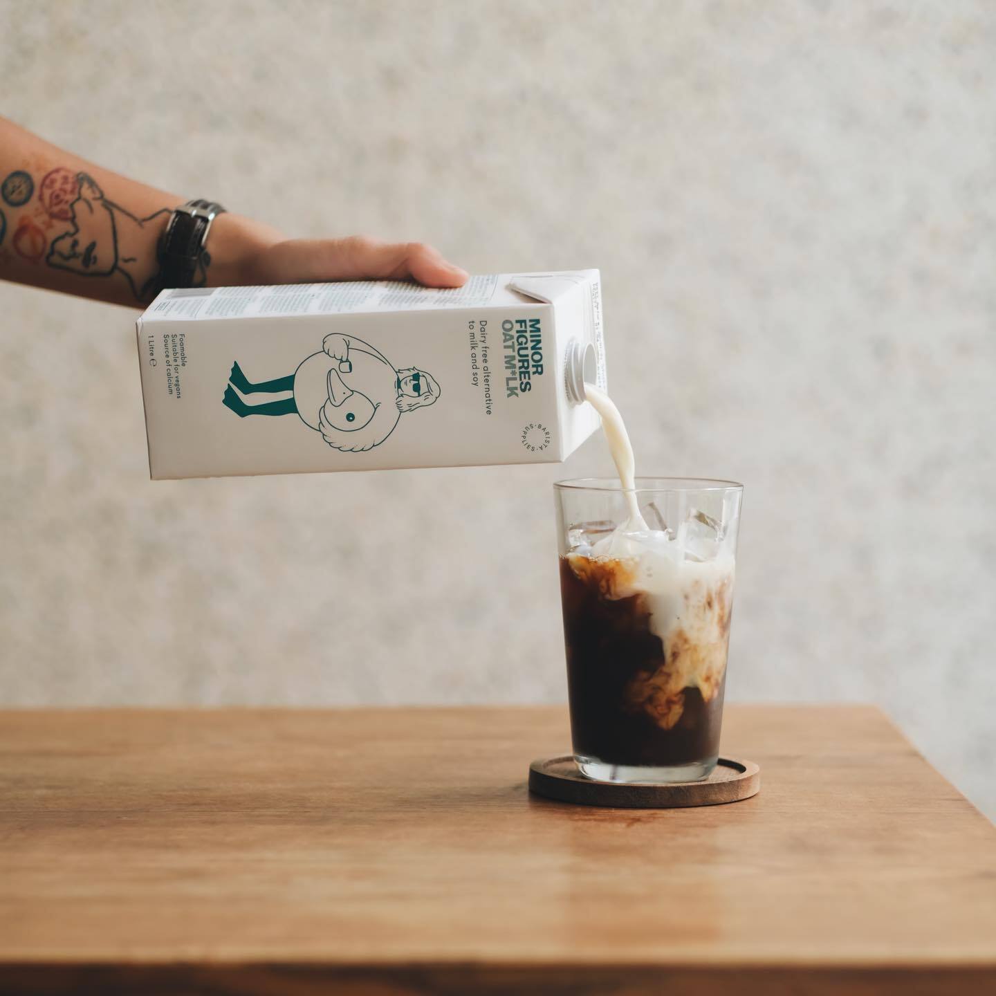 closeup of hand pouring minor figures barista oatmilk into a glass with coffee